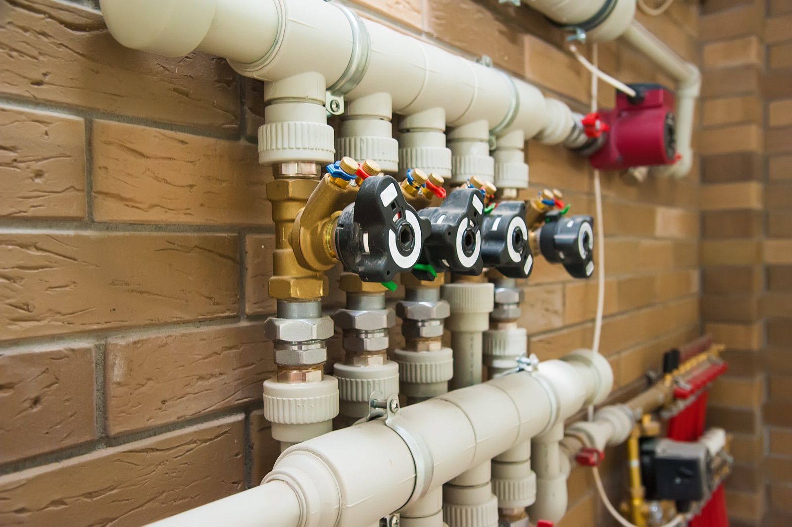 A manifold of pipes and shut-off valves mounted on a brick wall